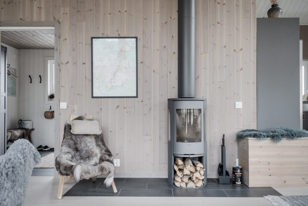 Grå kamin med vedförråd mot väggen i ljus träpanel i 1360 Björnselet