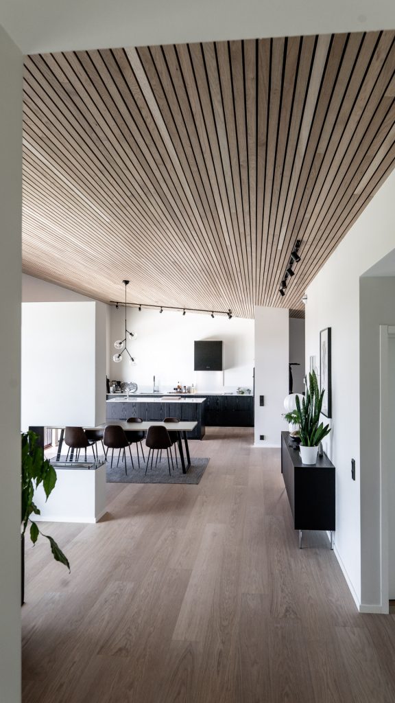 Hall i Villa Avaberg med ribbat trätak som leder mot kök och matplats