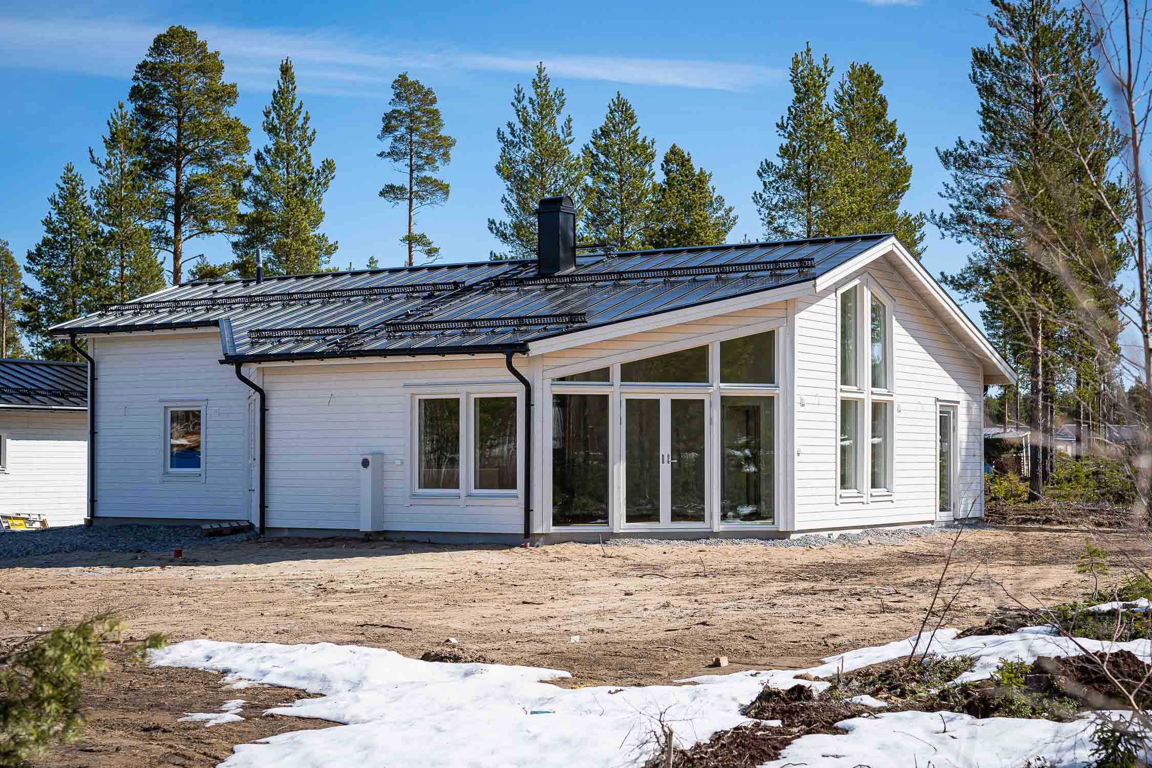 Vitt hus med svart plåttak och stora glaspartier bland tallar