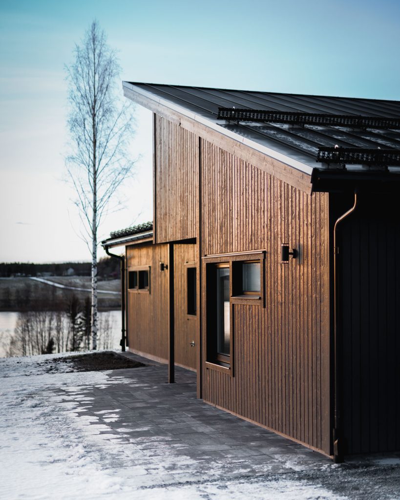 Villa Avan – brun träfasad och pulpettak med utsikt över vintrig sjö